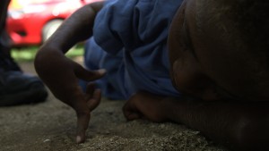 A young boy from Vanuatu lies on his side drawing in the sand with his finger